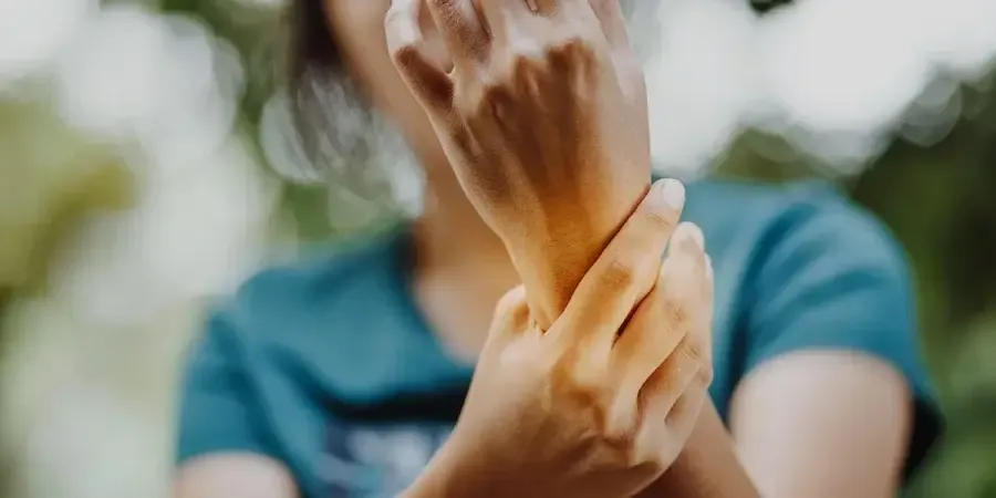 A woman in a blue t-shirt holds her left arm, which hurts, with her right hand