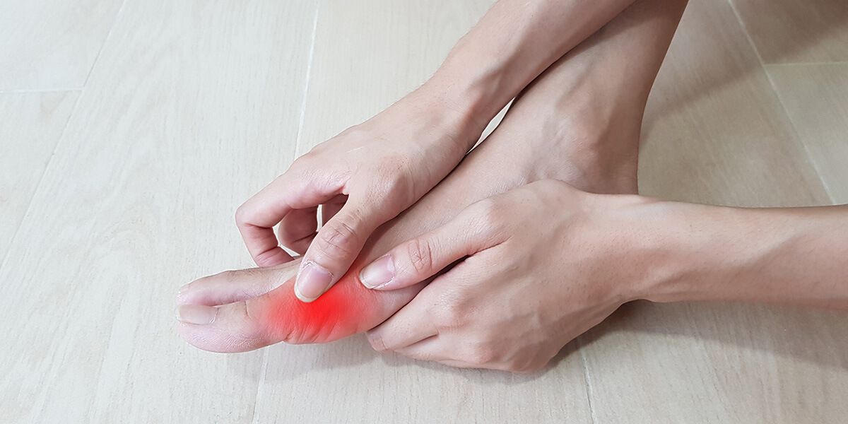 A woman holds on with her hands to her foot, which hurts from gout